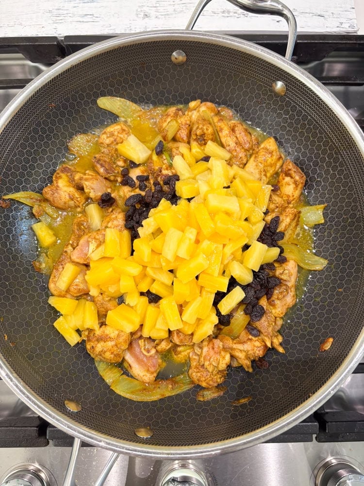 Once the chicken is fully coated/glazed, add the cream, water, salt, raisins, pineapple chunks, and half the almonds, if using.