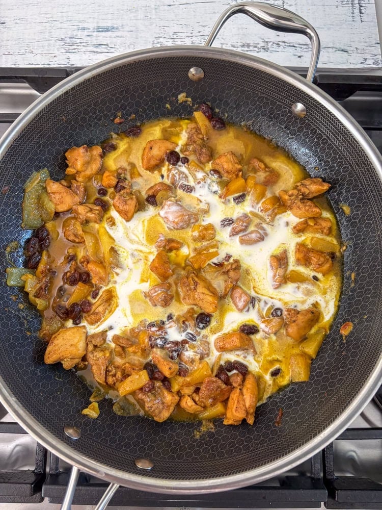 Once the chicken is fully coated/glazed, add the cream, water, salt, raisins, pineapple chunks, and half the almonds, if using.