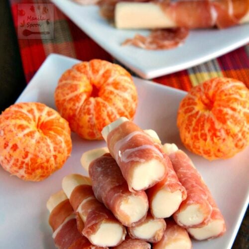 stack of prosciutto-wrapped mozarella sticks in a plate with oranges