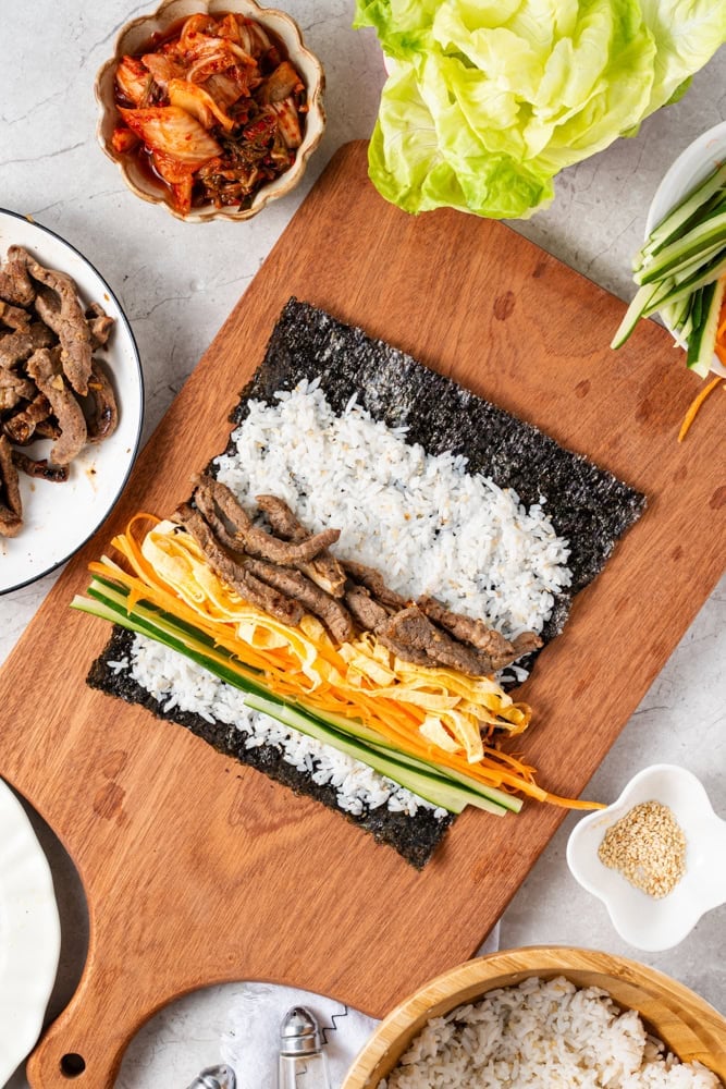 Arrange cucumber, carrot, egg slices, beef, and kimchi in rows across the rice.