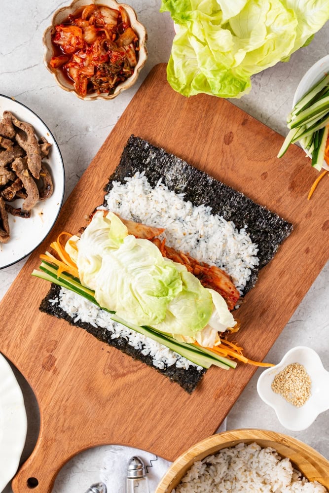 Arrange cucumber, carrot, egg slices, beef, and kimchi in rows across the rice.