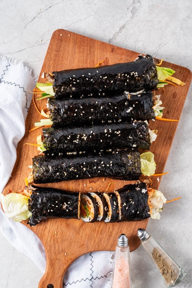 Starting from the bottom, roll the kimbap tightly while gently tucking in the fillings as you go. Lightly dampen the uncovered edge with water to seal the roll securely.